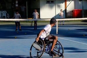 Alunos jogam tênis com menino na cadeira de rodas